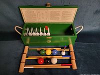Open green wooden case showing 6 wooden mallets with colored handles, 6 colored balls, and 6 white metal hoops inside the box