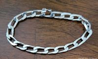 Full view of a sterling silver curb link bracelet with flat and slightly twisted links on a wooden surface.
