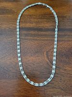 Full view of the 18 inch sterling silver serpentine link chain necklace laid flat on wooden surface.