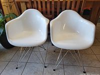 Pair of white molded plastic armchairs with chrome bases, showing full front view and seating area.