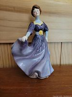 Front view of Royal Doulton Jacqueline figurine in purple dress with yellow accents on wooden shelf
