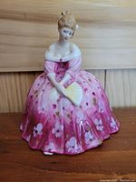 Front view of the Royal Doulton figurine Victoria HN 2471 showing a lady in a pink floral dress holding a fan, placed on a wooden surface.