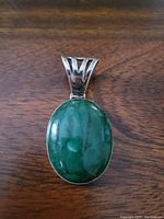 Front view of the sterling silver pendant showing the polished green aventurine oval stone and silver setting on a wooden background.