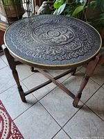 Full view of assembled folding tea table showing round carved top and X-frame legs