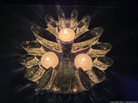 Angled overhead view of the glass trivit hot plate lit with three tea light candles, showing the clear textured glass petals and round base.
