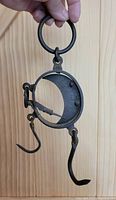 Metal circular hanging scale with hook and ring handle, showing signs of vintage wear and patina