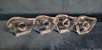 Four clear glass napkin rings shaped as birds arranged in a line.