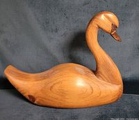 Full side view of the wooden swan decoy showing smooth curves and detailed carving with natural wood grain visible.