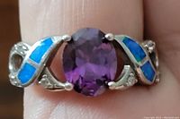 Front view of the sterling silver ring showing the oval amethyst gemstone centerpiece flanked by blue opal inlays and crystals.