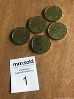 Five 1986 Canadian one dollar coins arranged on a surface with a Maxsold lot number card. Coins show patina and the Voyageur canoe design.