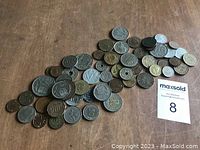 Photo showing a broad assortment of over 50 European coins spread out on a wooden surface in mixed metals and sizes.