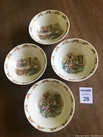 Four Bunnykins bone china bowls with rabbit border and interior Bunnykins scenes, displayed on wood surface