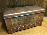 Closed front view showing walnut veneer grain pattern and curved lid profile.