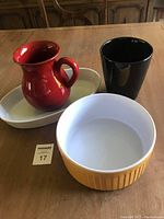 Full lot overview showing four ceramic kitchenware items: red pitcher, black cup, white oval dish, yellow souffle baking dish bowl.