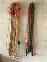 Photo showing two long extension cords (orange and yellow) and a hooked metal chain hanging vertically against a wooden wall.