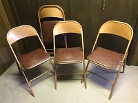 Four vintage Cooey folding card table chairs standing upright, showing bronze colored frames and brown padded seats.