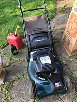 Front view of Craftsman lawn mower showing 21-inch cutting deck, grass catcher bag, and fuel containers on the ground nearby.