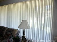Curtains fully extended across living room window behind lamp and sofa.
