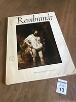 Front cover of the 1954 Rembrandt art print book showing a famous Rembrandt painting of a man standing with his feet in water, dressed in white, part of his signature artistic style.