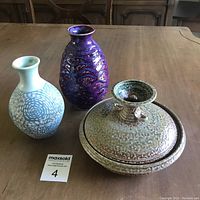 Three assorted Canadian studio pottery pieces on wooden table. Purple vase, blue and white patterned vase, and a green/brown lidded pottery dish.