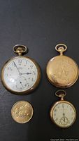 Photo showing three pocket watches with one large Eaton watch, one smaller Waltham without case parts, and one smaller Law L Moore watch with engraved back, also includes a coin for scale.