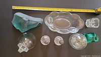 Top-down photo of all antique glass items showing size with measuring tape, includes Victorian oval dish, crystal bell, salt and pepper shakers, turquoise ink well, and etched turquoise glass piece