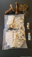 View of two large bags of assorted old white and cream buttons, Art Deco style hair comb, wooden darning tool, and two glass phials of beads on black surface.