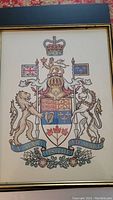 Close-up view of the framed Canadian Coat of Arms showing detailed heraldic elements and colors beneath glass.