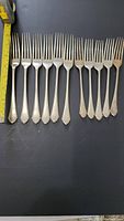 Eleven hallmarked silver forks arranged in a row with measuring tape showing largest fork length (~19 cm).