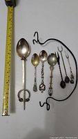 Full view of all 7 silver items showing spoons and pickle forks with a measuring tape for size reference