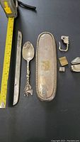 Photo showing the tape measure and several scrap silver items including the long metal strip, decorative spoon, and rectangular tray.