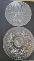 Overhead photo of two clear glass pedestal cake plates showing leaf and geometric starburst patterns