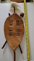 Full view of Zulu raw hide shield with attached horsehair plume, alongside spear and knobkerry, with measuring tape showing length approximately 30 inches.