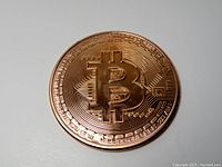 Front side of the copper Bitcoin coin showing large Bitcoin symbol and circuitry design.