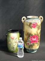 Photo showing two vintage decorative vases next to a water bottle for size reference, highlighting the taller vase with pink roses and ornamental handles and the smaller green floral vase.