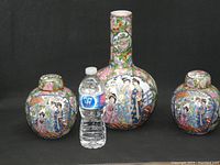 Three pieces of Famille Rose Chinese pottery including two lidded jars and one tall vase with detailed hand-painted figure and floral designs.