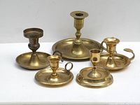 Five brass candle holders in varying vintage styles placed on white background, showing varying patina and wear.