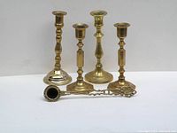 All four brass candle holders and brass candle stuffer arranged together on white background