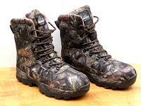 Pair of Itasca women's waterproof hunting boots in camouflage seen from front-side angle on wooden surface.