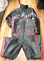 Full view of black Angora motorcycle leather jacket and pants with stripe detailing laid out on floor.