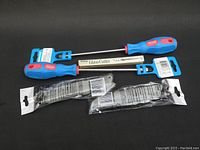 Two glass cutters with blue and red handles laid flat, with two packaged utility knives below them on a black surface.