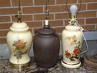 Three vintage ceramic table lamps in varying styles and finishes, placed side by side against a brick background.