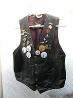 Front view of vintage black leather vest with multiple enamel pins and buttons attached, showing front details and interior color.