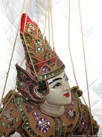 Close-up of marionette's head showing detailed wood carving, traditional painted face, and conical sequined hat.