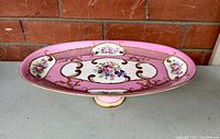 Angled front view of the pink and gold elevated platter with visible floral details.