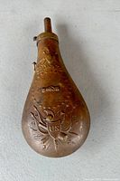 Top view of the brass powder flask showing the embossed patriotic design including 'US' shield and crossed flags.