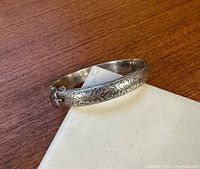 Full view of the sterling silver cuff bangle showing the floral engraved design and hinged cuff shape.