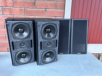 Pair of Mission bookshelf speakers without grilles, revealing 2 large woofers and 1 smaller tweeter per speaker inside black cabinet