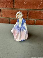 Front view of Royal Doulton Dinky Do porcelain figurine showing detailed dress in blue and pink and bonnet.