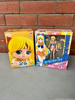 Two boxed Sailor Venus figures from Sailor Moon, side by side against brick background